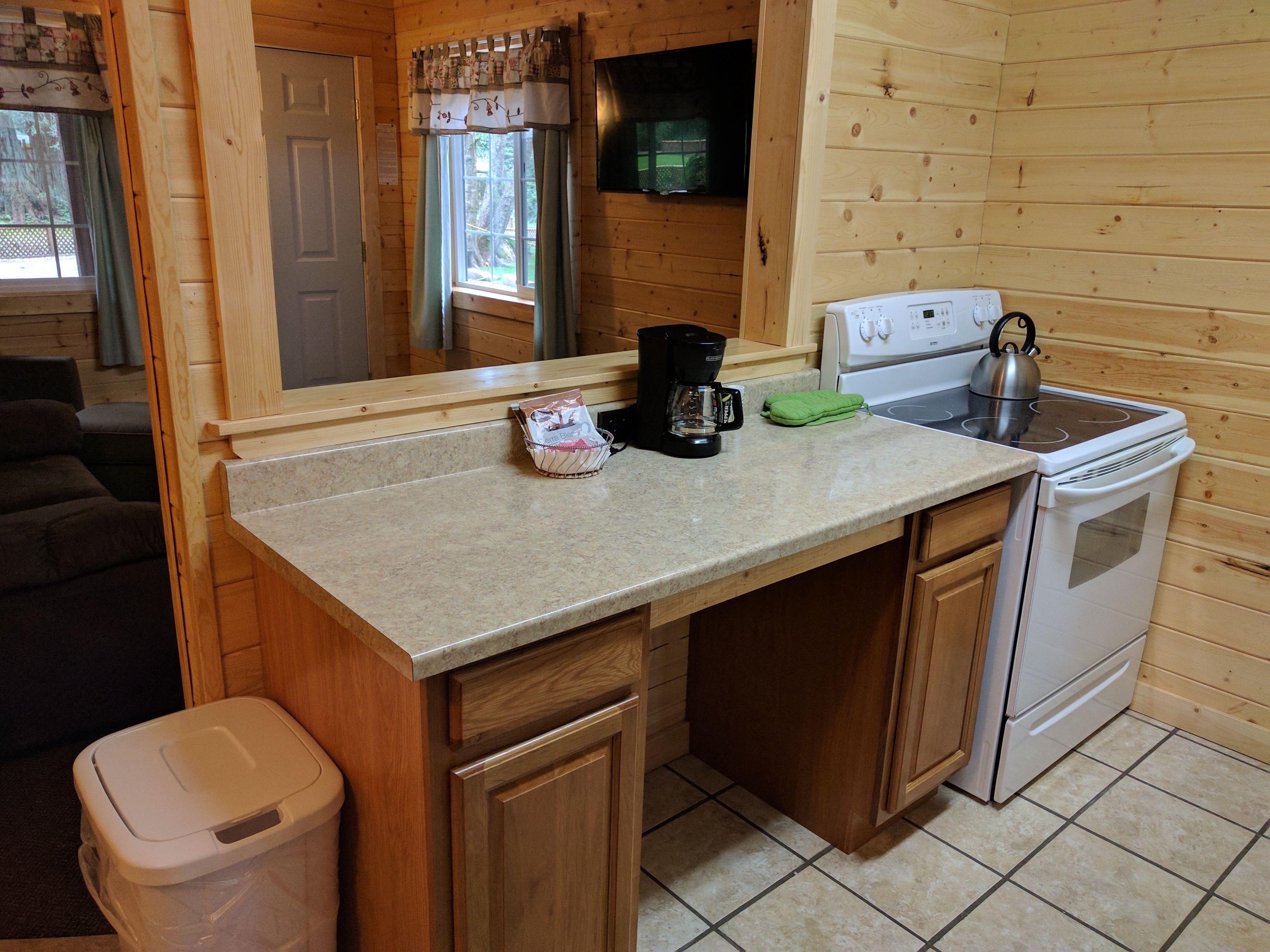 A compact kitchen with wooden cabinets, a countertop, a stove, and a coffee maker.