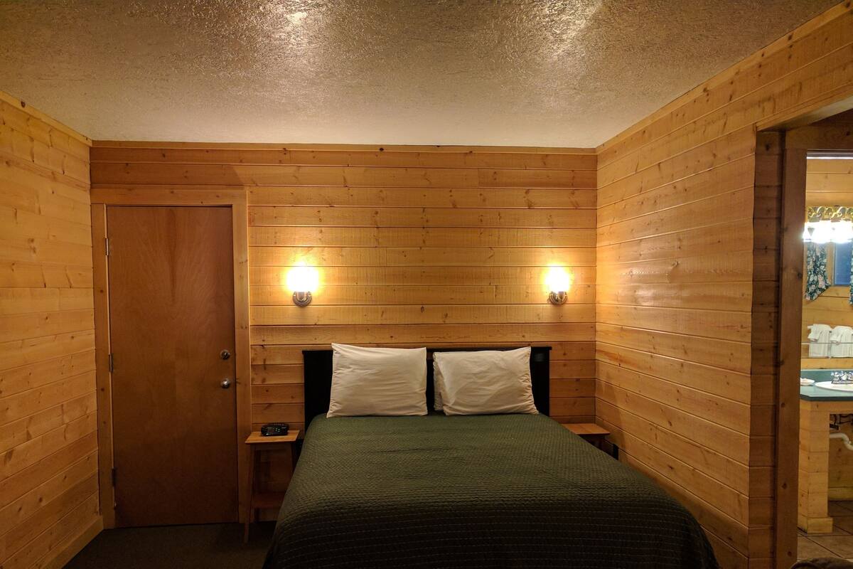 A wooden-paneled room with a bed, two bedside lamps, and a door.