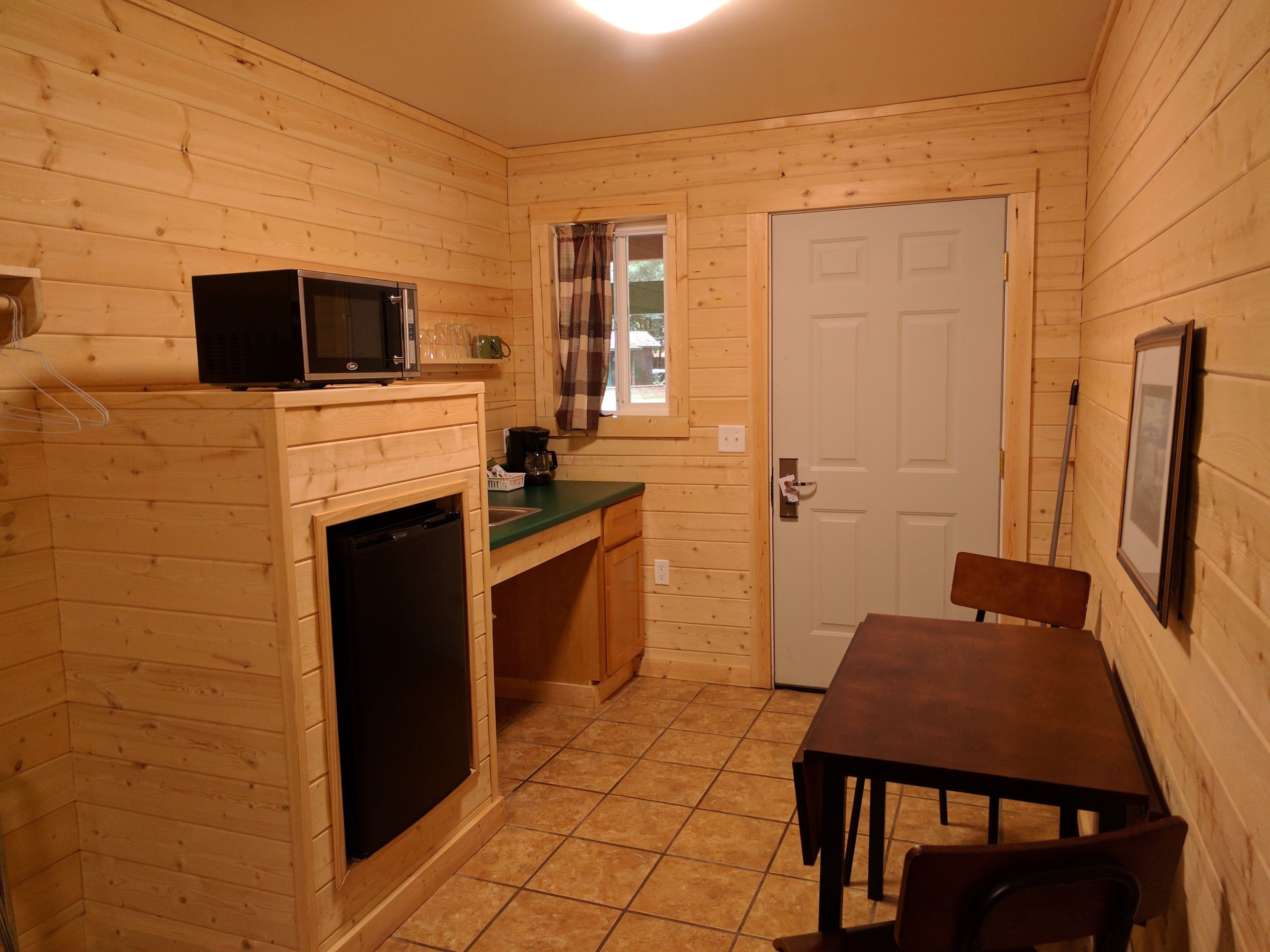 A compact kitchen with wooden walls, a microwave, a sink, and a small dining area with a table and chairs.