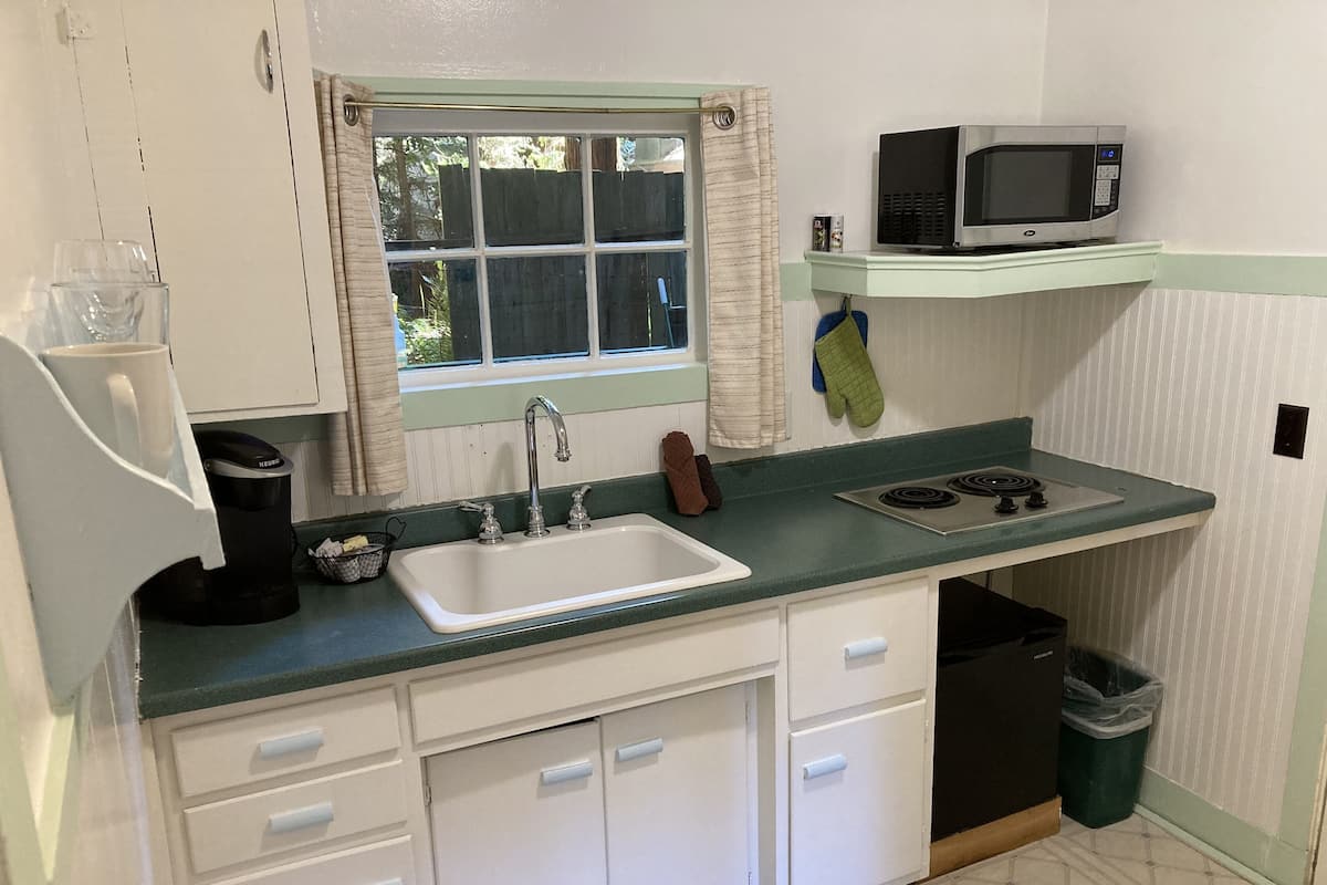 A compact kitchen with a white sink, a stove, and a microwave on a green countertop.
