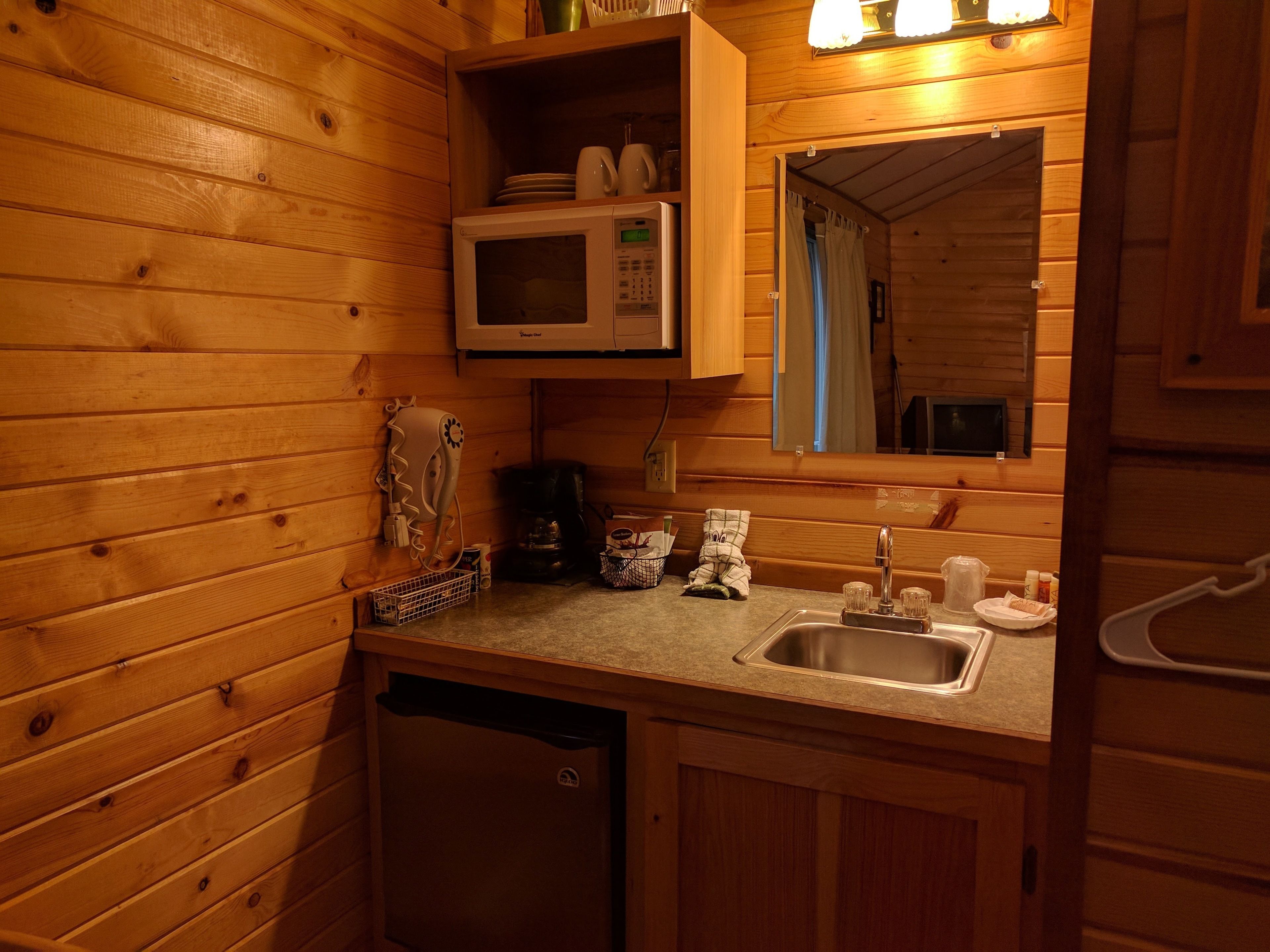 A compact kitchen with wooden walls, a microwave, a coffee maker, and a sink.