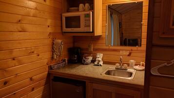 A compact kitchen with wooden walls, a microwave, a coffee maker, and a sink.