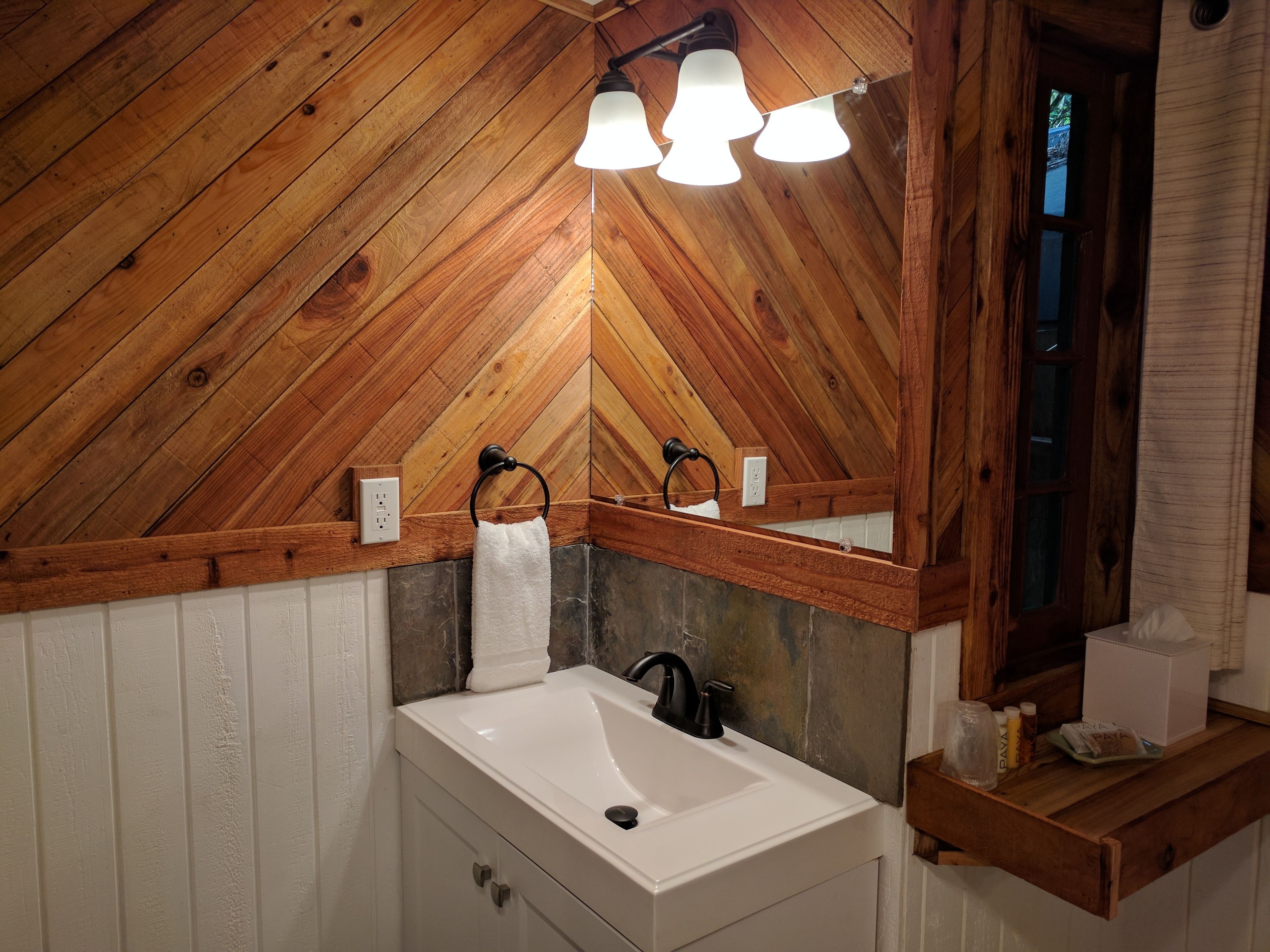 A bathroom with a wooden ceiling, a white sink, and a mirror.