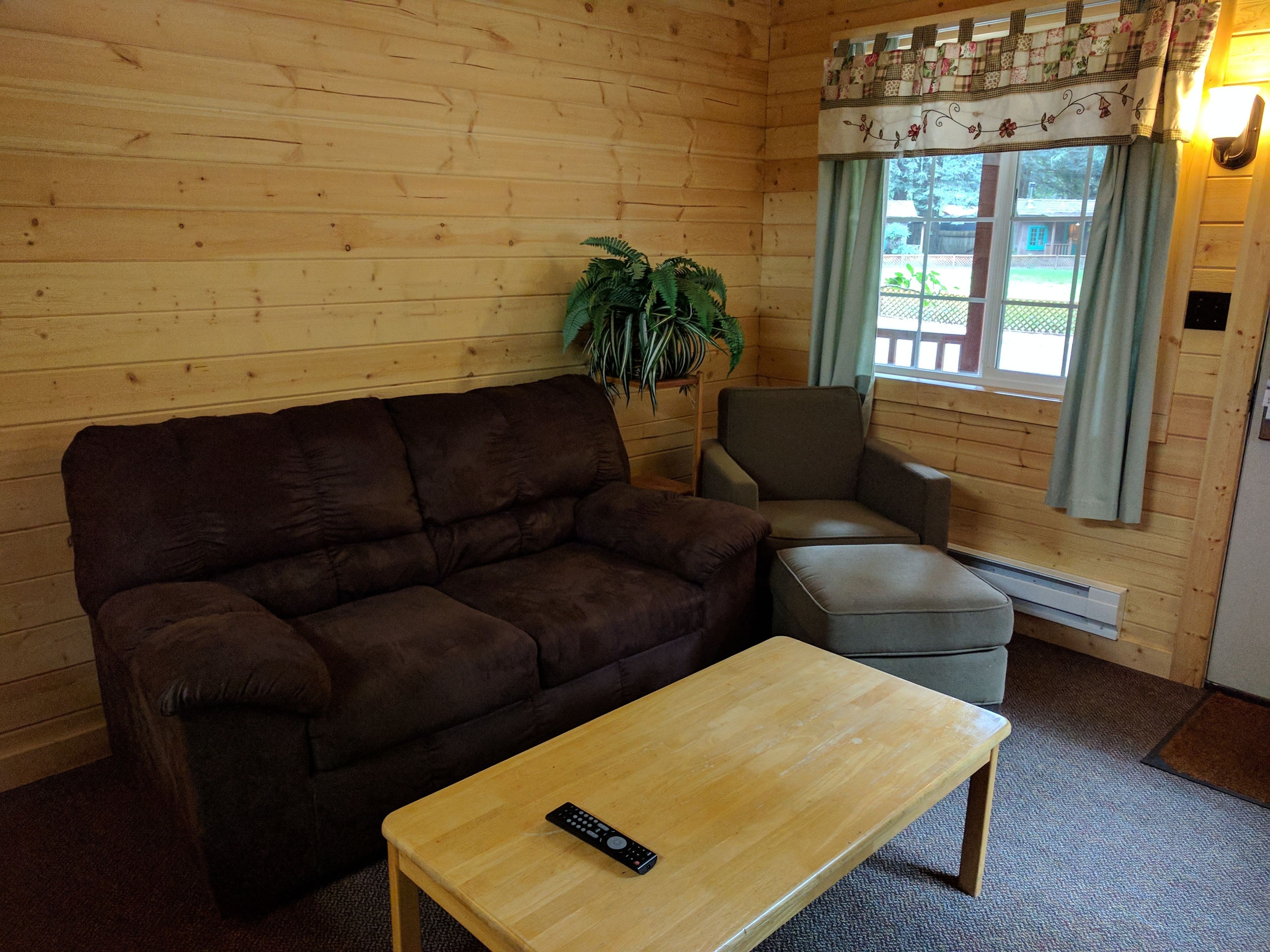 A cozy room with a brown sofa, a wooden coffee table, a grey armchair, and a potted plant.