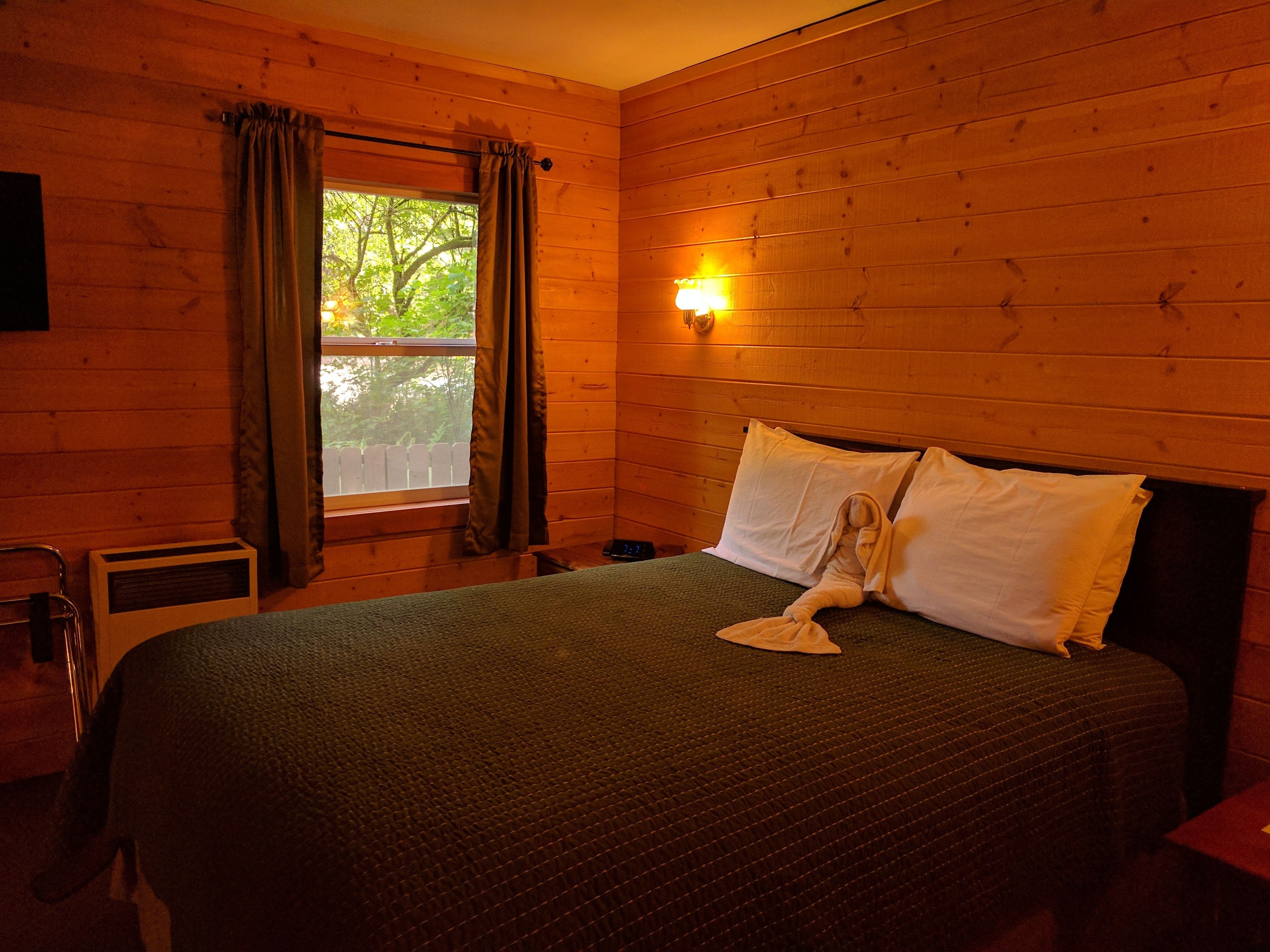 Een kamer met houten lambrisering, een bed, een raam met gordijnen, een wandlamp en een radiator.