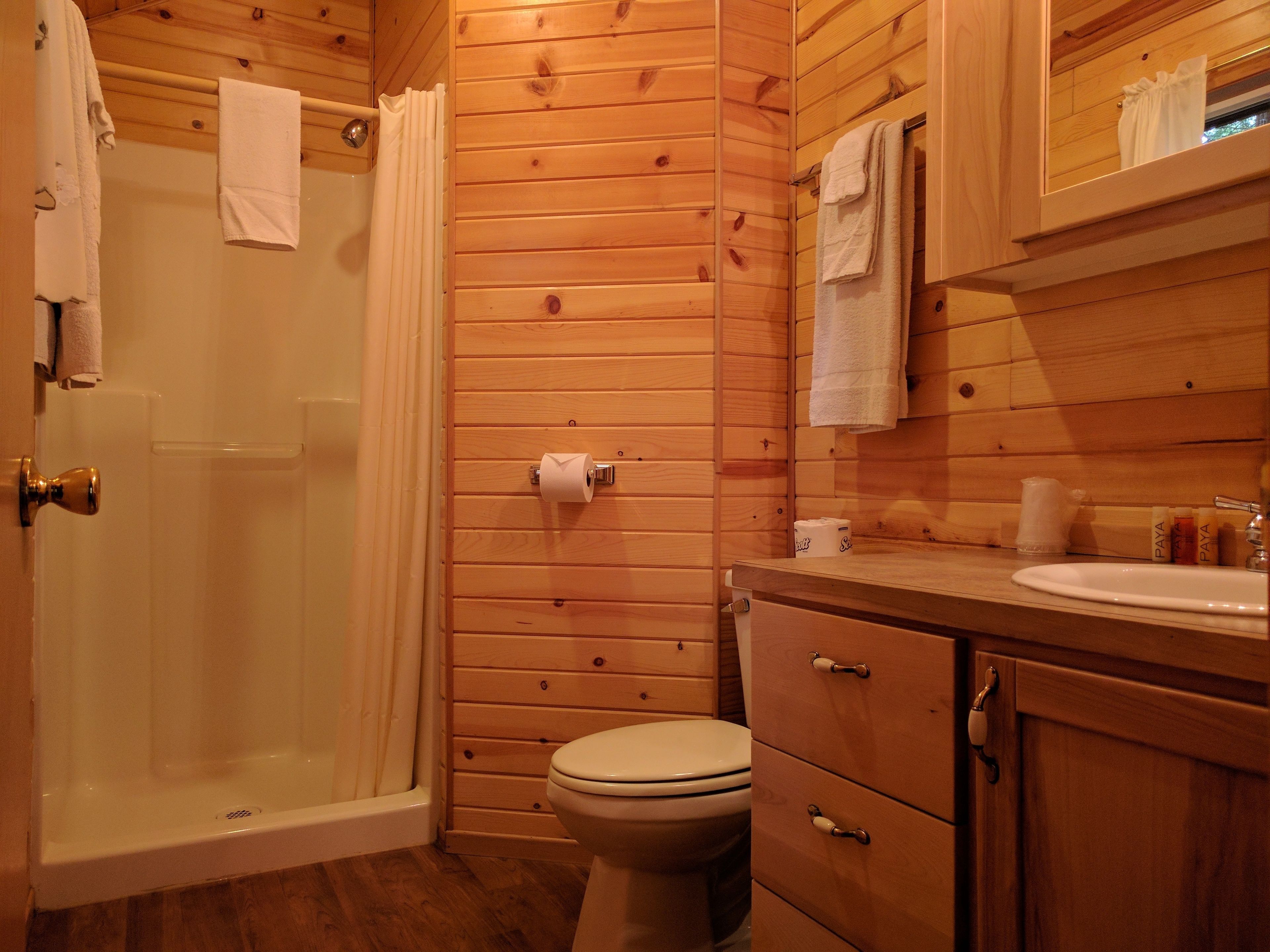 A wooden-paneled bathroom with a shower, toilet, and sink.
