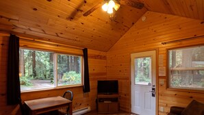 Interior de una cabaña con piso de madera, una mesa de comedor con sillas, televisor y un sofá.
