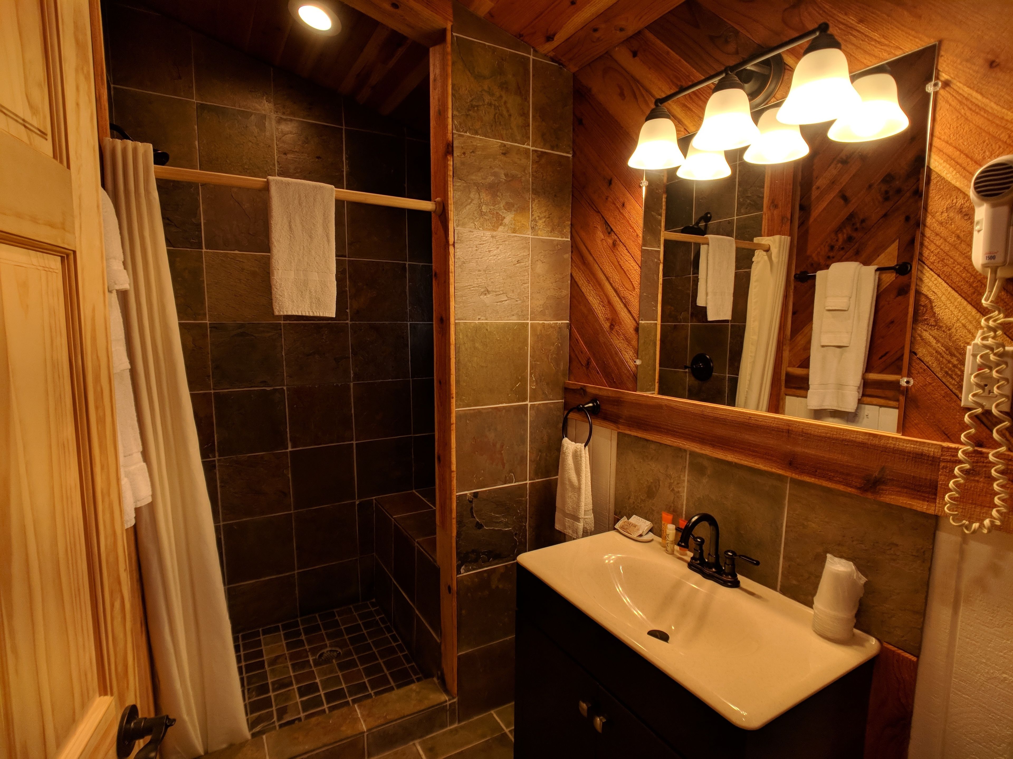 Un baño con ducha, lavamanos y espejo con iluminación.