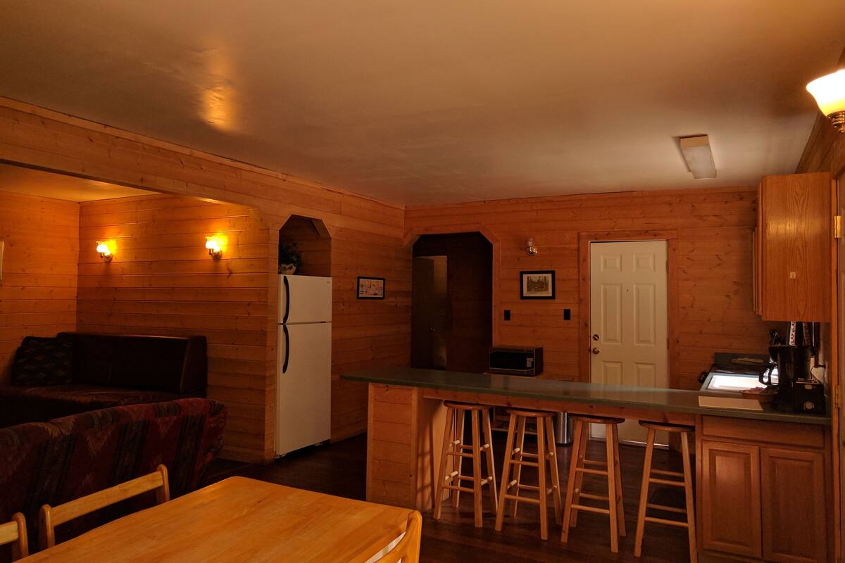 A cozy kitchen with wooden walls, a refrigerator, a microwave, and a bar area with stools.