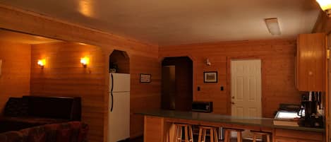 A cozy kitchen with wooden walls, a refrigerator, a microwave, and a bar area with stools.