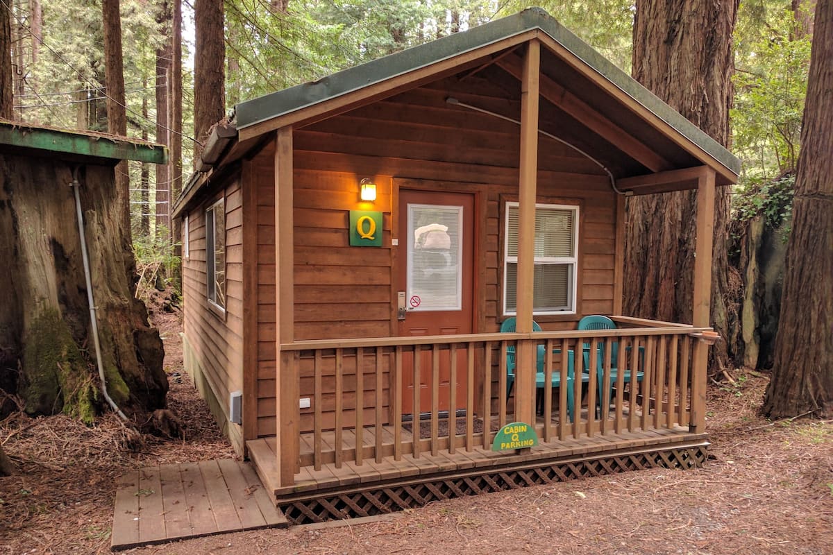 A small cabin with a porch, a door with a window, and a sign indicating it is a cabin and parking area.