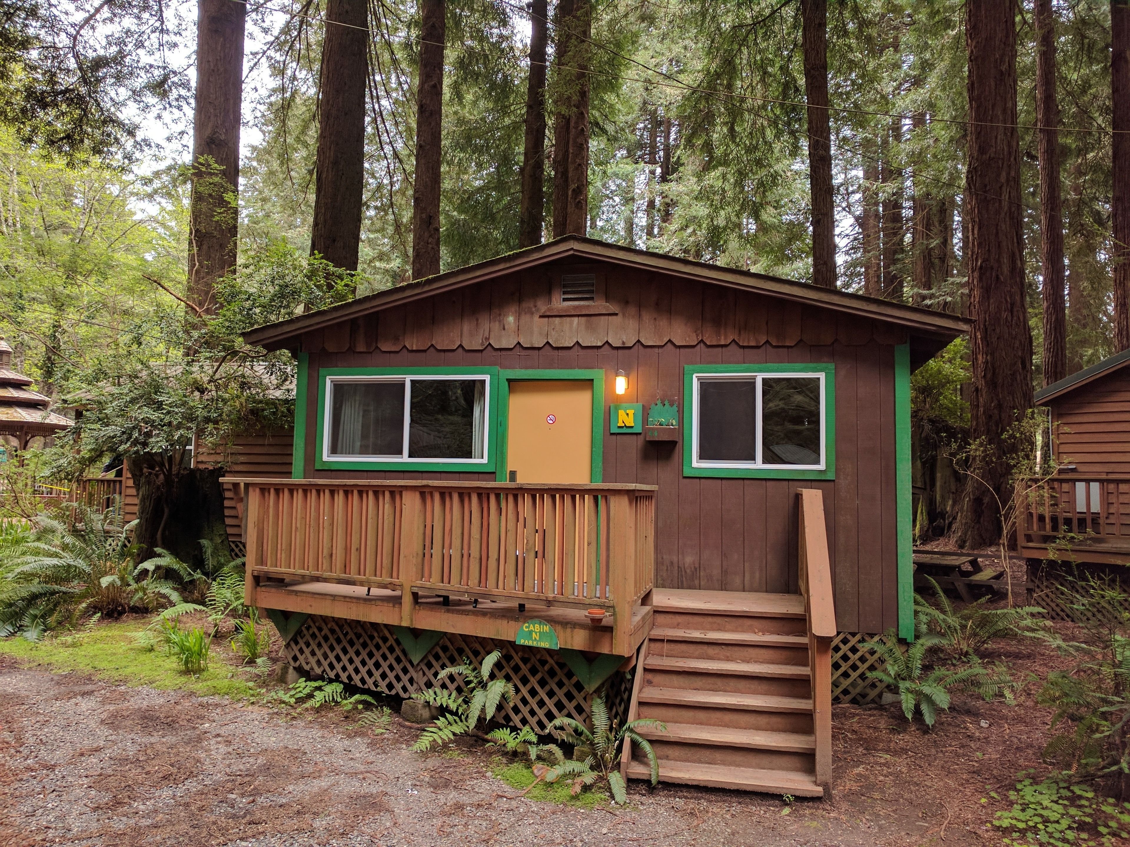 A cabin with a wooden deck, a set of stairs, and a sign indicating it is a cabin with parking.