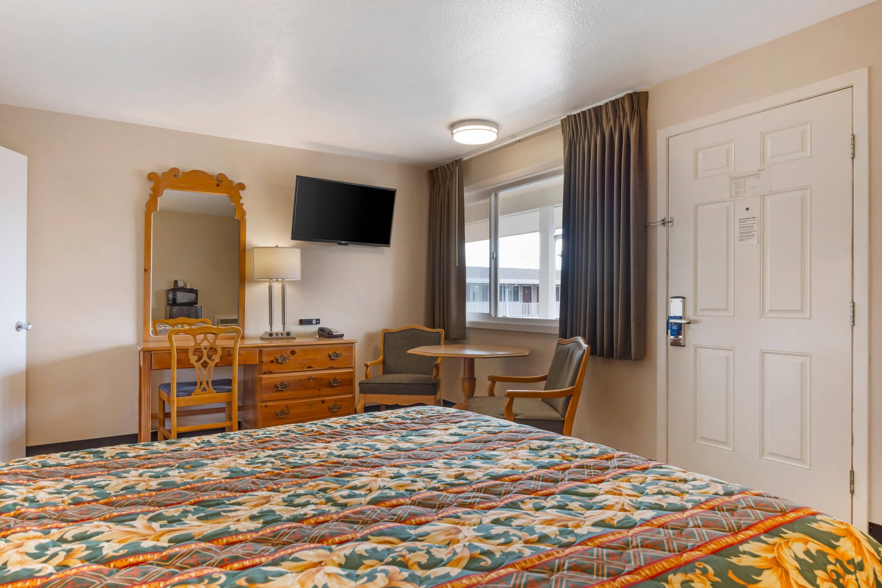 A hotel room with a large bed, a desk with a chair, a television, and a window with curtains.