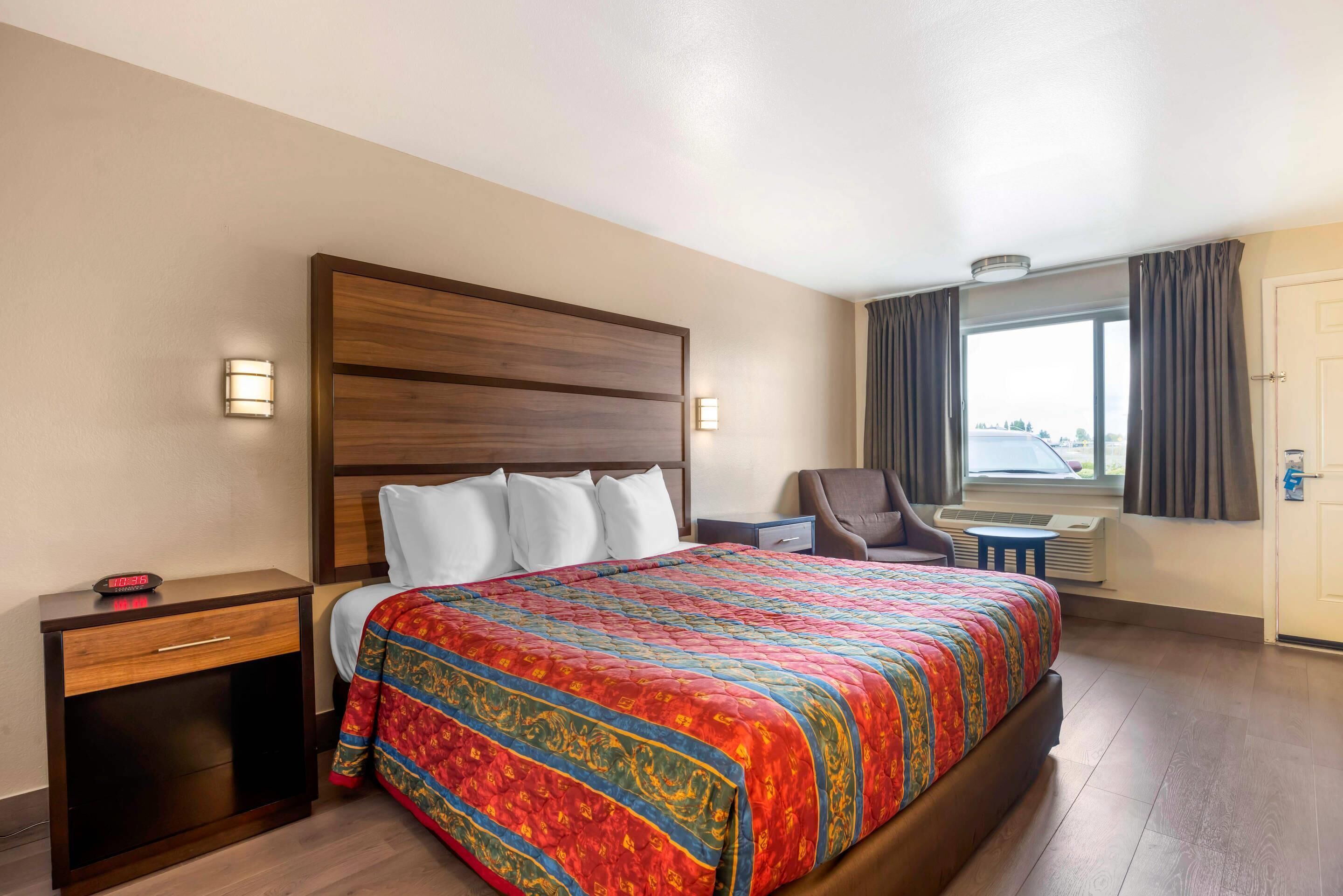 A hotel room with a large bed, a nightstand, a chair, a small table, and a window with curtains.