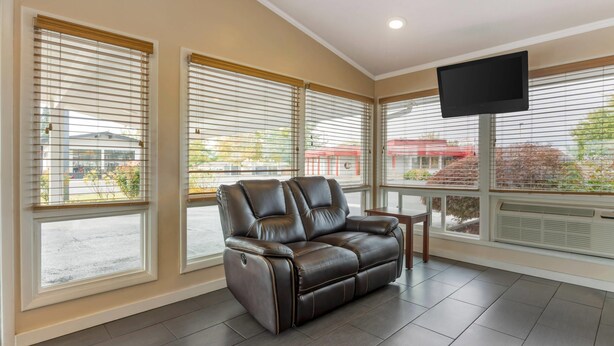 A modern living room with a leather sofa, large windows with blinds, a flat-screen TV, and a small table. - Rodeway Inn Albany (Albany)