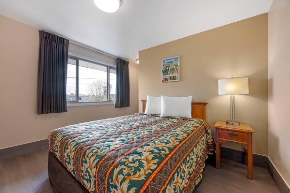 A hotel room with a large bed, a nightstand with a lamp, a window with curtains, and a wall decoration. - Rodeway Inn Albany (Albany)