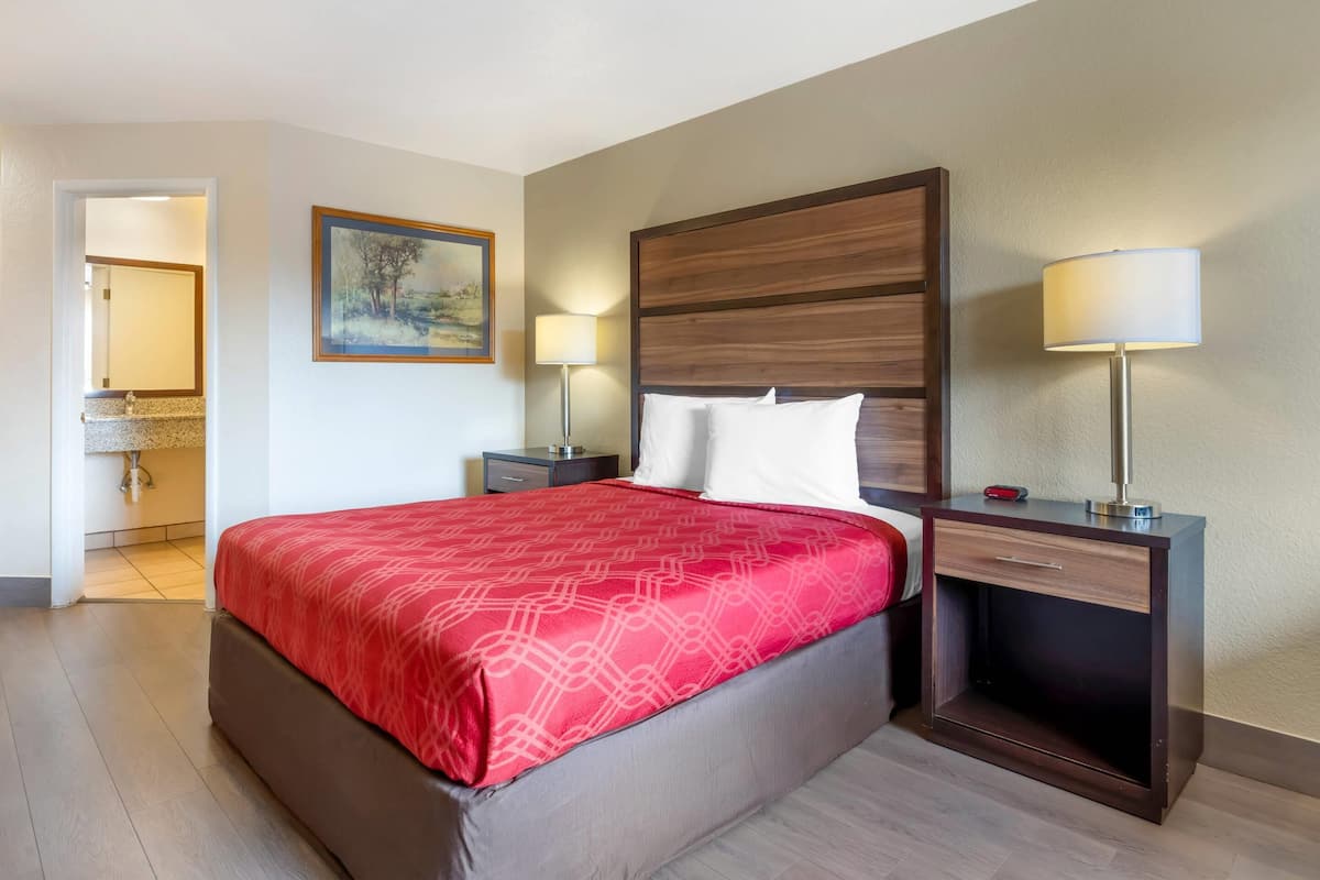 A hotel room with a large bed, two bedside tables, a nightstand, a painting on the wall, and a lamp on each table.