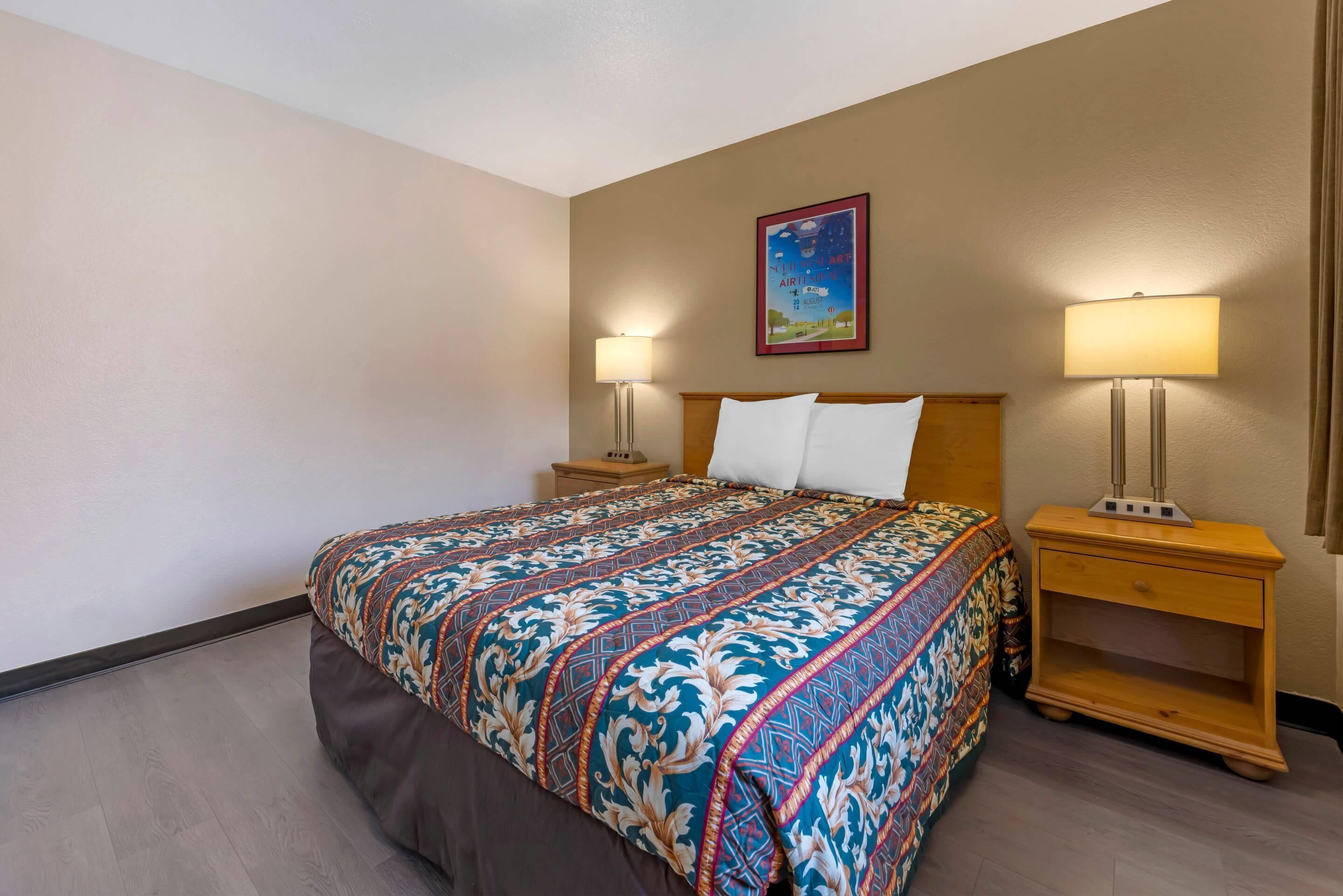 Habitación de hotel con una cama grande, dos mesitas de noche y una lámpara de pared.