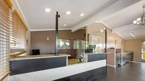 A hotel reception area with a modern design, featuring a reception desk, a seating area, and a large mirror reflecting the room. - Rodeway Inn Albany (Albany)
