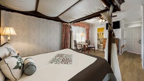 Una cama con dosel y cuatro columnas, un cabecero decorativo, una mesita de noche con lámpara y vistas a un baño con una pared de acento amarillo.
