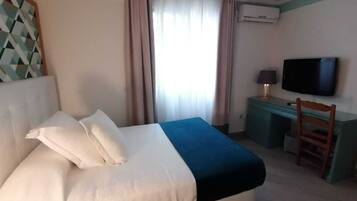 A hotel room with a bed, a desk, a chair, a television, and an air conditioning unit.