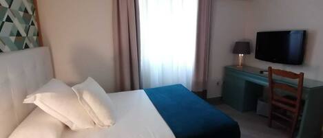 Una habitación de hotel con cama, escritorio, silla, televisor y aire acondicionado.