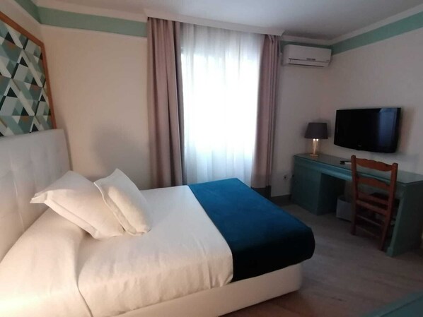Una habitación de hotel con cama, escritorio, silla, televisor y aire acondicionado.