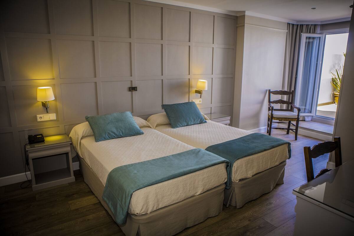 Ein Hotelzimmer mit zwei Betten, Nachttischlampen, einem Sessel und einem Schreibtisch.