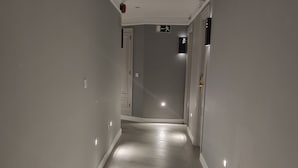 Un couloir étroit et bien éclairé, doté d’un plancher en bois et de murs blancs, avec un panneau de signalisation et des luminaires encastrés.