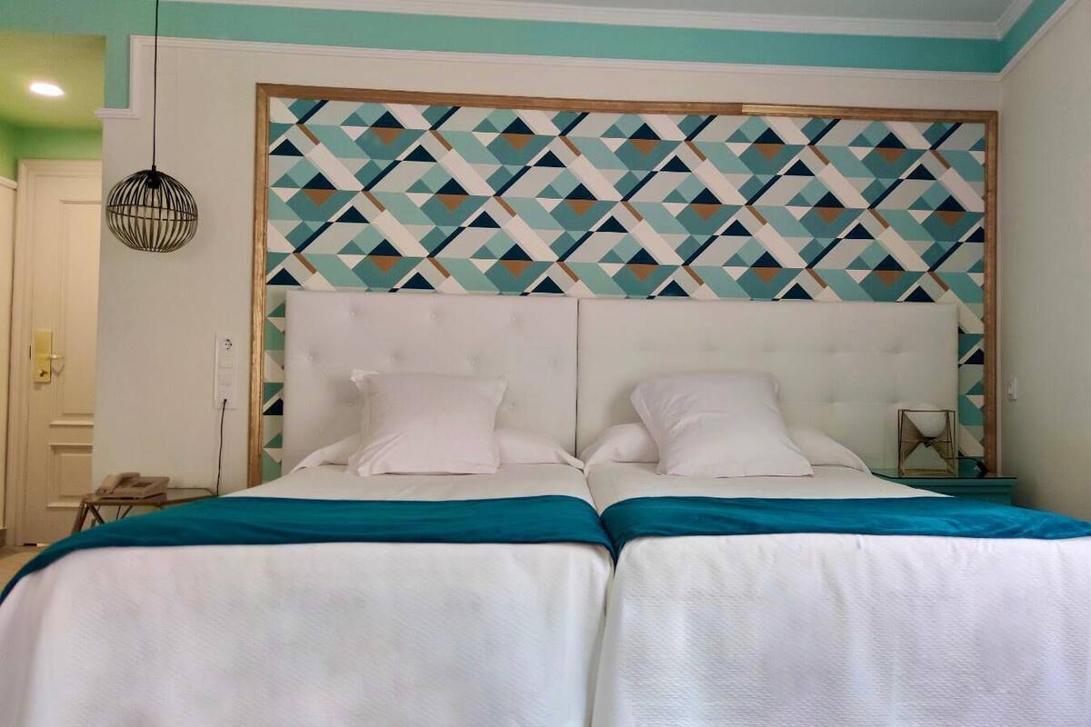Ein Doppelbett mit einem Kopfende im geometrischen Muster, weißer Bettwäsche und Türkis-Akzenten.