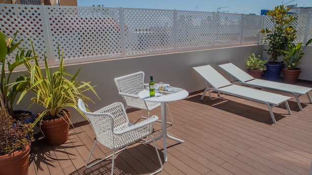 Une terrasse sur le toit, avec une table et deux chaises, entourée de plantes en pot et d’une clôture blanche en treillis.
