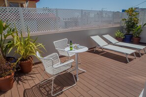 Eine Dachterrasse mit Tisch und zwei Stühlen, umgeben von Topfpflanzen und einem weißen Gitterzaun.