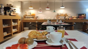 Une table dressée pour le petit-déjeuner avec des croissants, des kiwis, des fraises, une tasse de café et un verre de jus d’orange.