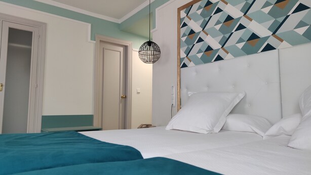 Een slaapkamer met een bed, witte beddengoed, een hoofdbord met een geometrisch patroon en een hanglamp.