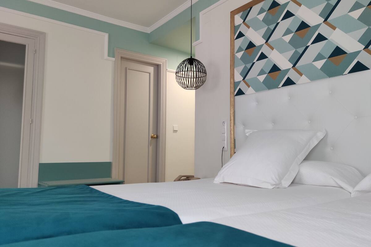 Ein Schlafzimmer mit Bett, weißer Bettwäsche, einem Kopfende mit geometrischem Muster und einer Pendelleuchte.