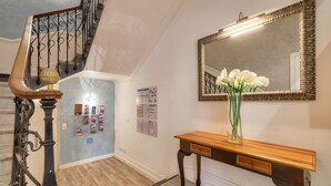 Un escalier orné de rampes en métal, une console en bois avec un miroir et un vase rempli de fleurs blanches.