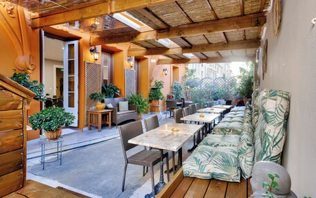 An outdoor patio with wooden tables and chairs, a sofa, and potted plants.