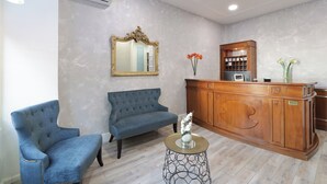 Un espace d’accueil avec un canapé bleu, un comptoir d’accueil en bois, un miroir et un vase rempli de fleurs.