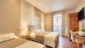 Une chambre d’hôtel avec deux lits, un bureau en bois, une chaise, une télévision et un balcon avec vue.