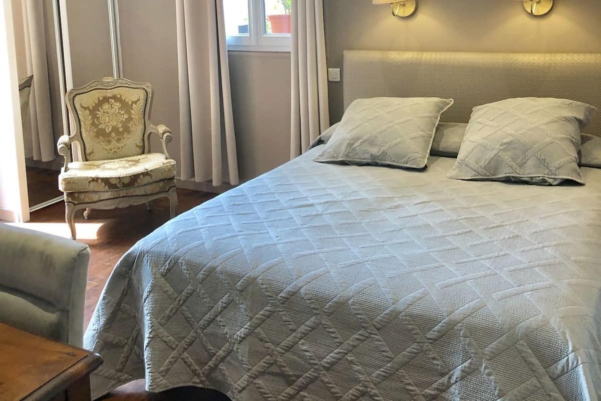 A bedroom with a bed, two bedside lamps, a chair, and a window with curtains.