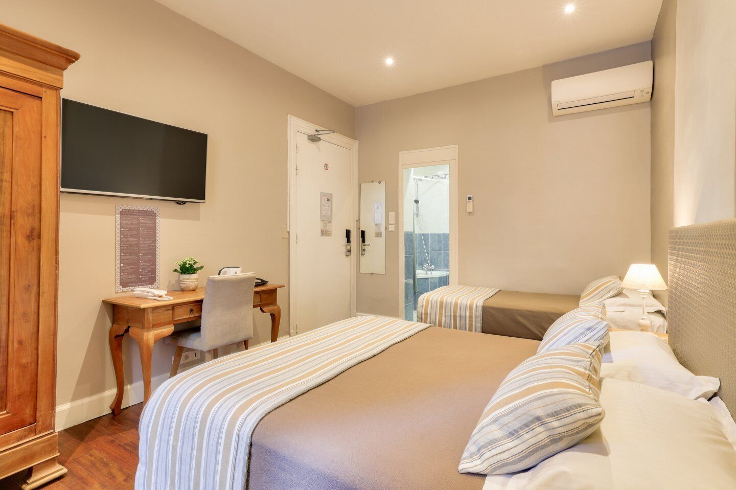 A hotel room with a bed, a desk, a chair, a television, and an air conditioning unit.