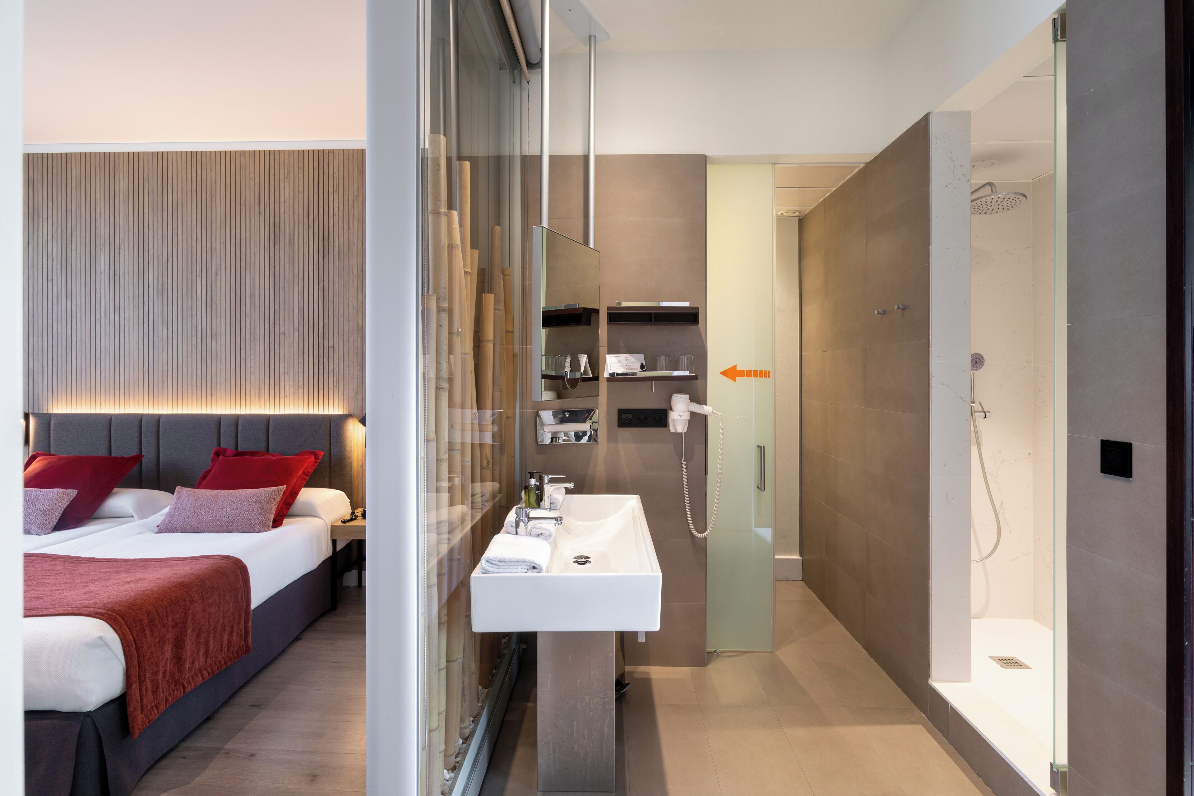 Ein modernes Hotelzimmer mit Bett, Bad mit Glasdusche und integriertem Waschbecken.