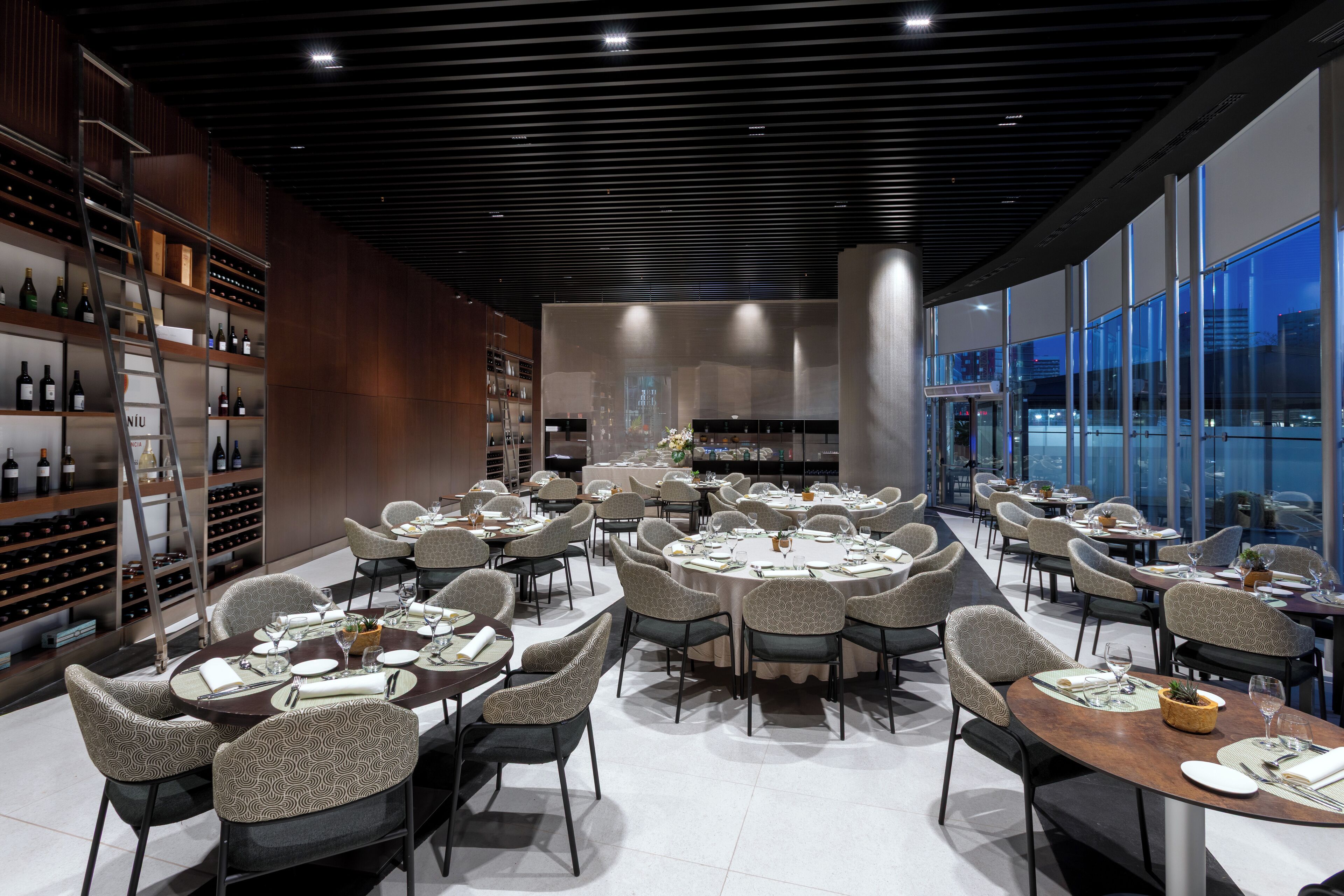 A modern dining area with round tables, chairs, and a wine rack.