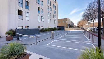 Un estacionamiento con espacios delimitados, un edificio con múltiples ventanales y un cielo despejado.