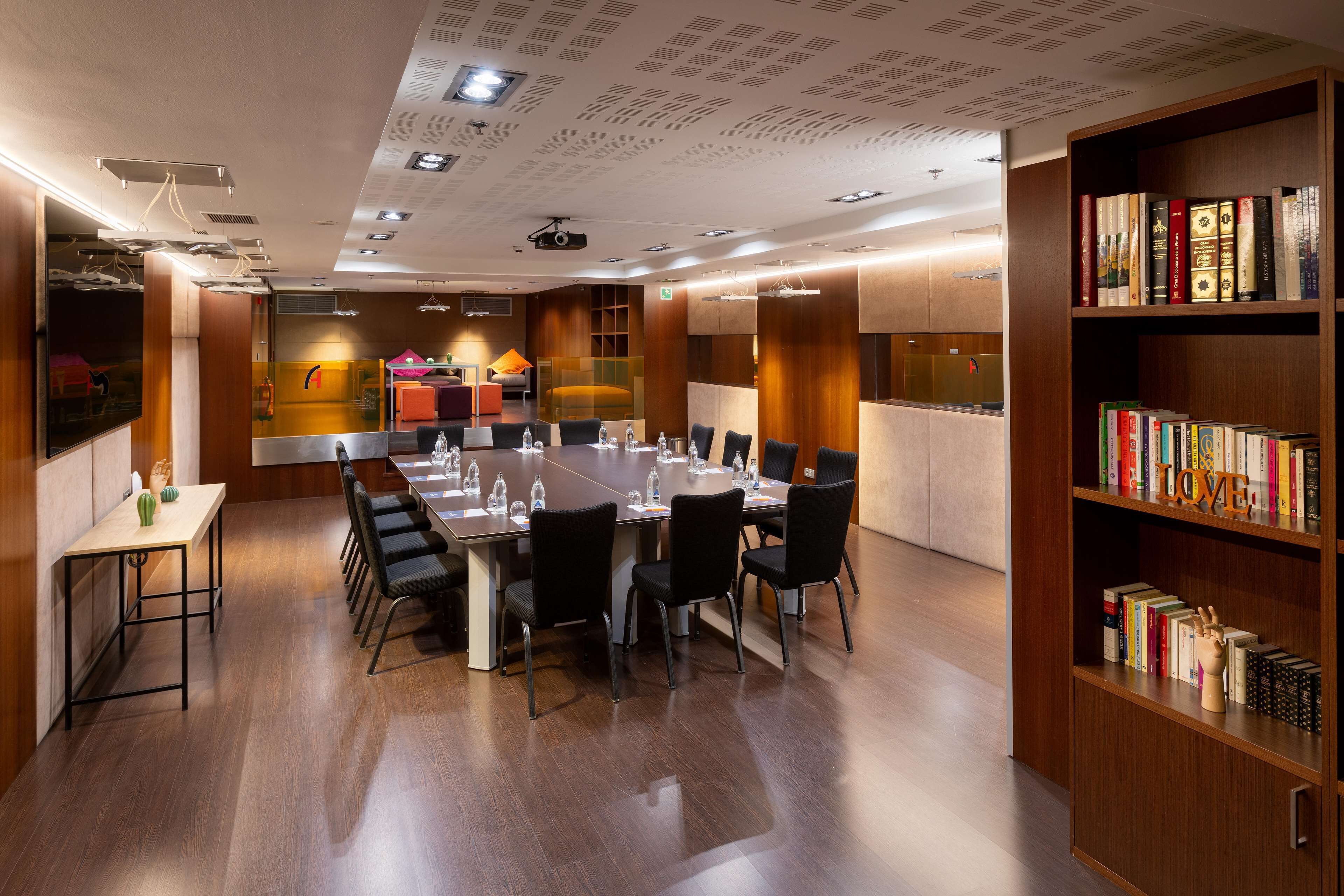 A conference room with a long table, black chairs, and a bookshelf filled with books.