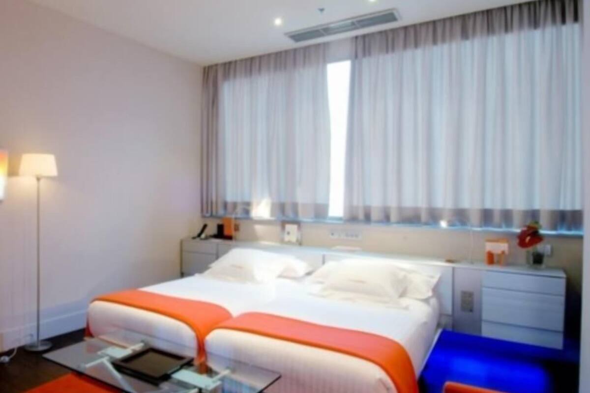 A hotel room with a bed, bedside table, lamp, and a window with curtains.