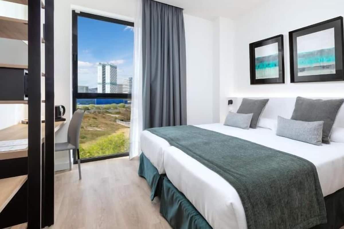 A modern hotel room with a large bed, a desk, and a view of the city.
