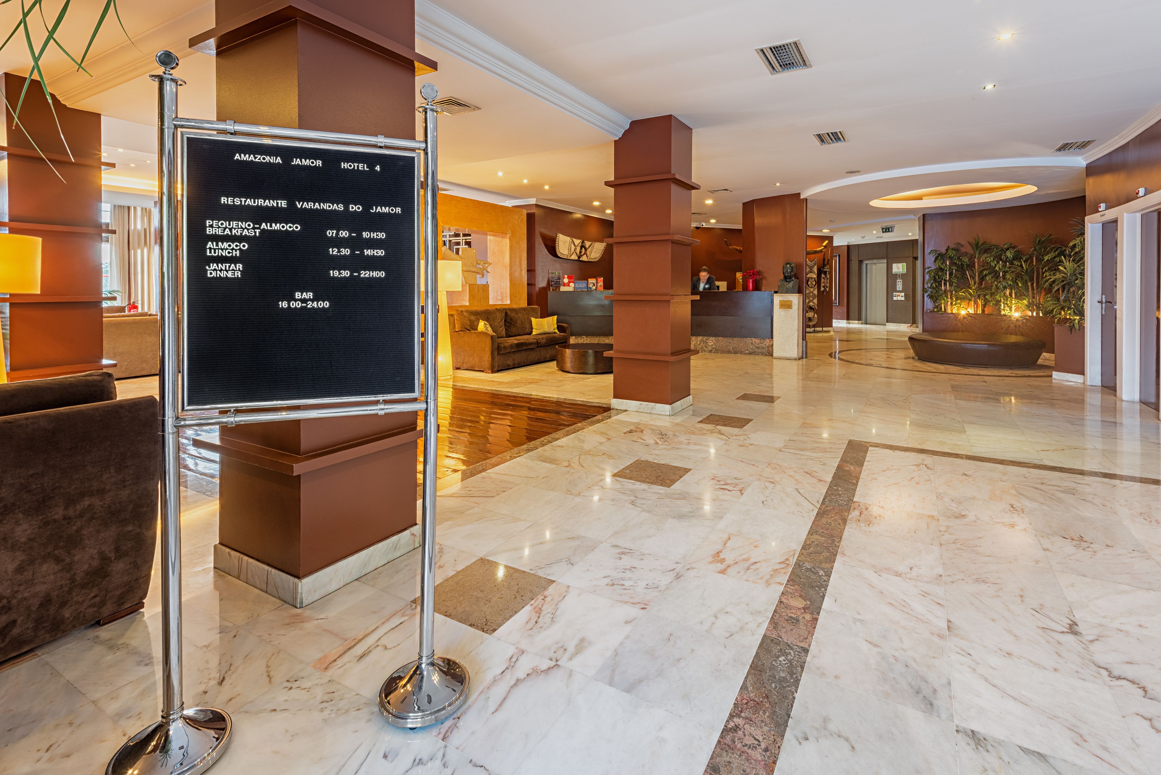 Un hall d’hôtel comprenant un comptoir d’accueil, une horloge, un canapé et un panneau indiquant les heures d’ouverture du restaurant.