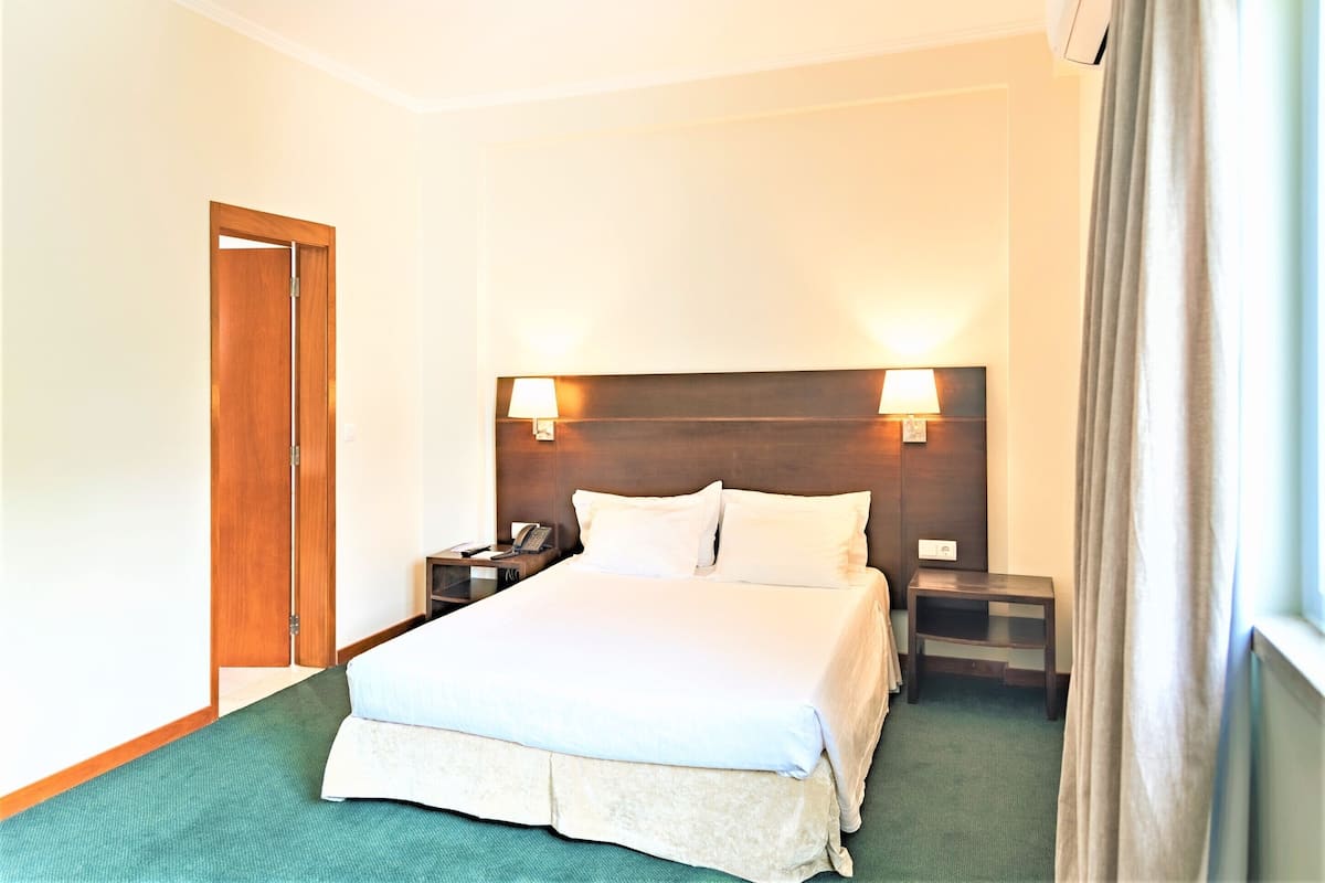 A hotel room with a large bed, two bedside tables with lamps, a wooden headboard, and a green carpet.