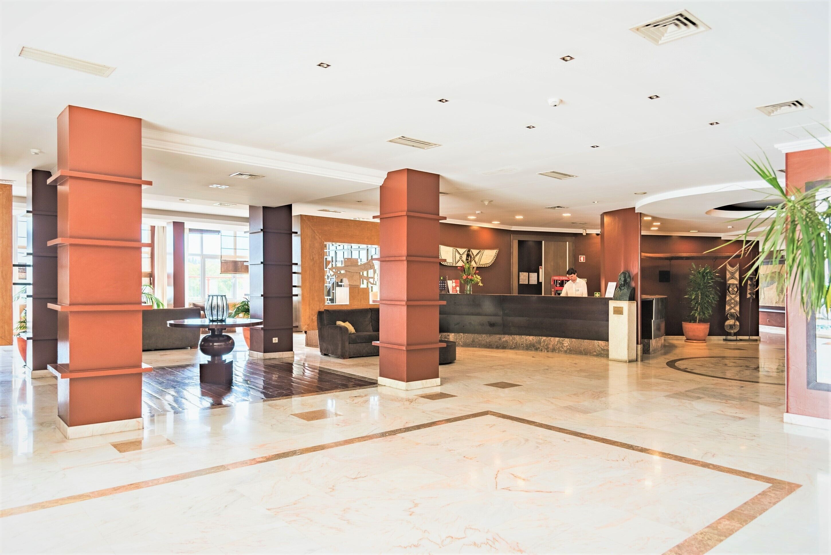 A spacious lobby with a reception desk, large pillars, and a polished marble floor.